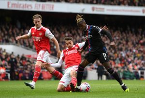 Arsenal debutante Jakub Kiwior makes a block on Crystal Palace winger Wilfred Zaha while fellow defender Rob Holding watches from a distance during a league match played at the Emirates on Sunday 19th March 2023.